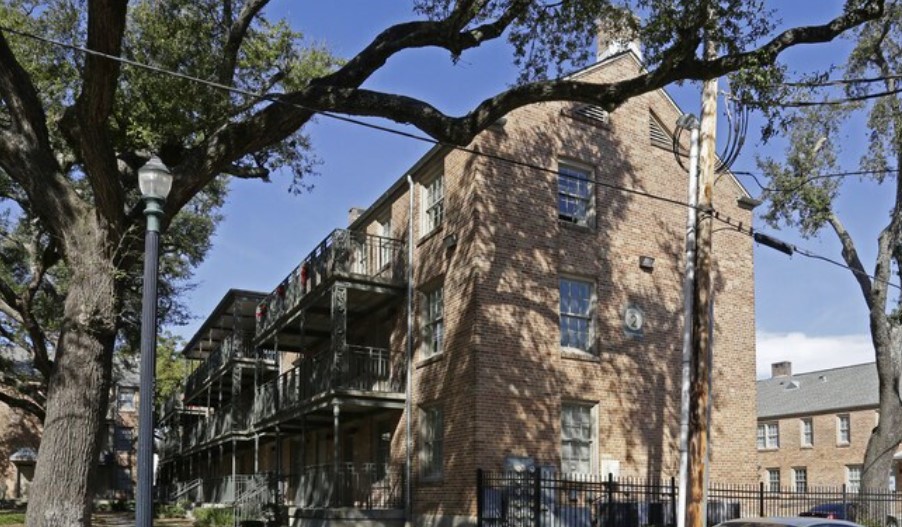 A tree in front of a building with a balcony.